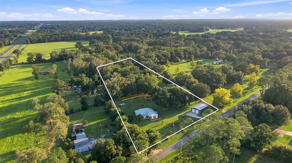 An aerial view shows a house and detached garage on a large, tree-lined rural lot — 1050 NE 165TH STREET, CITRA, FL