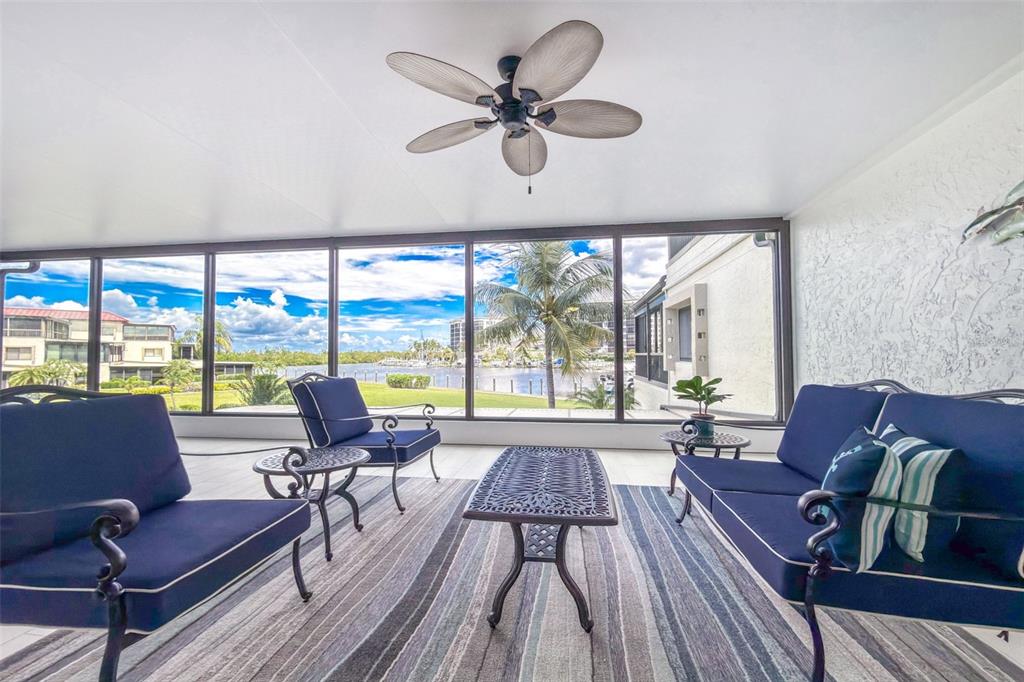 A sunroom with blue patio furniture, a ceiling fan, and large windows overlooking a waterway — 3250 SOUTHSHORE DRIVE UNIT 55B, PUNTA GORDA, FL