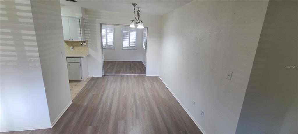 A dining area with wood-look flooring leads into a kitchen and a sunroom with shutters — 9901 111TH LANE, SEMINOLE, FL