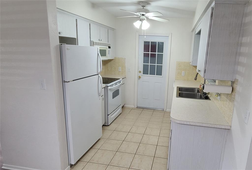 A kitchen features white cabinets, white appliances, tile flooring, and a door leading outside — 9901 111TH LANE, SEMINOLE, FL