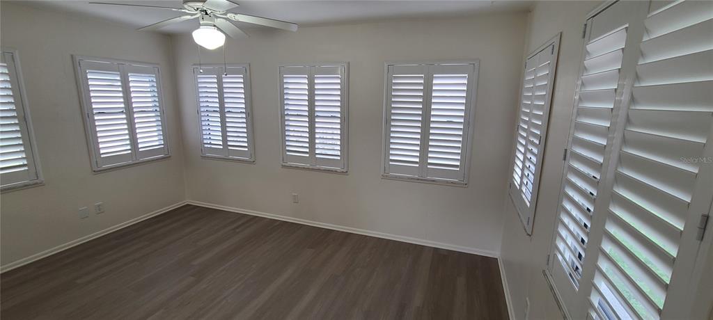 A room with light-colored walls, wood-look flooring, a ceiling fan, and white plantation shutters — 9901 111TH LANE, SEMINOLE, FL