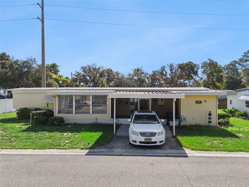 A yellow single-story mobile home features a carport with a white car parked underneath — 20 HAWAIIAN WAY, LEESBURG, FL