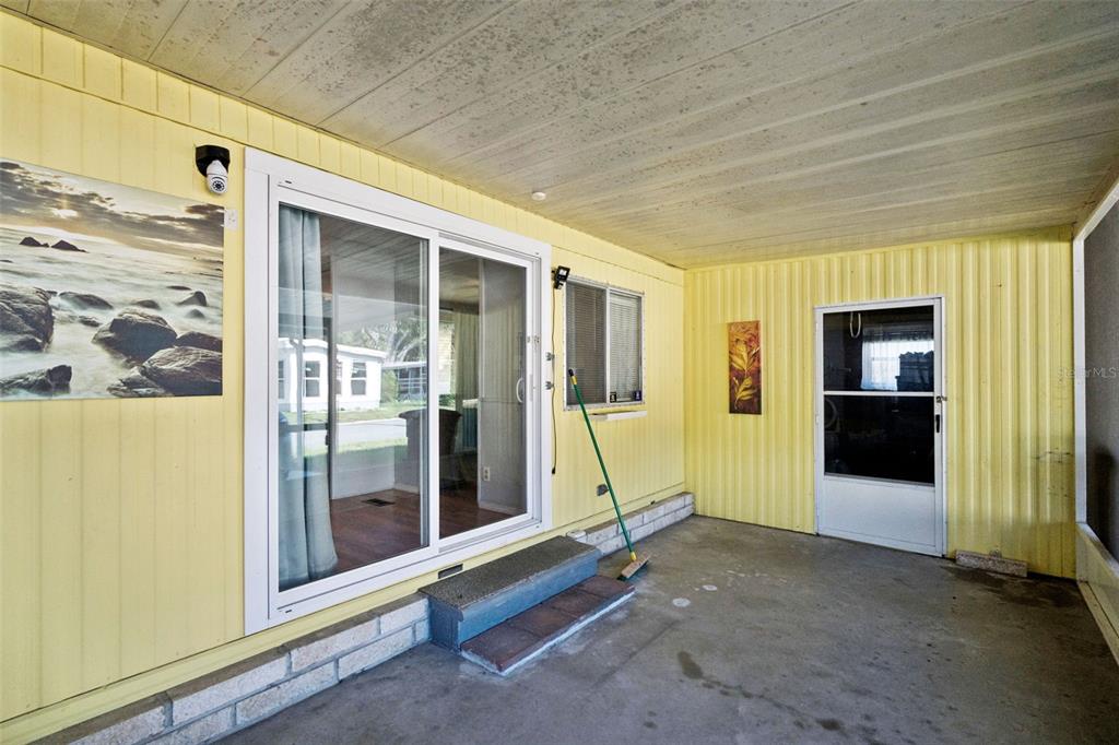A covered patio features yellow vertical siding, a sliding glass door, and a screen door — 20 HAWAIIAN WAY, LEESBURG, FL