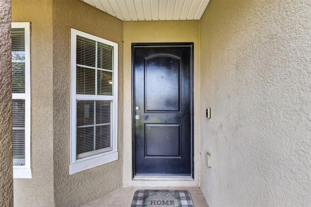 A black front door with a window to the left sits under a covered entryway — 702 CHELSEA AVENUE, FRUITLAND PARK, FL