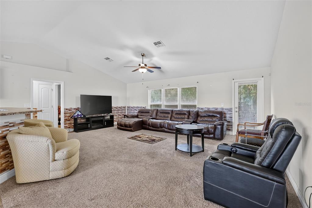 A spacious living room features a vaulted ceiling, brown leather sectional, and a tiled accent wall — 702 CHELSEA AVENUE, FRUITLAND PARK, FL