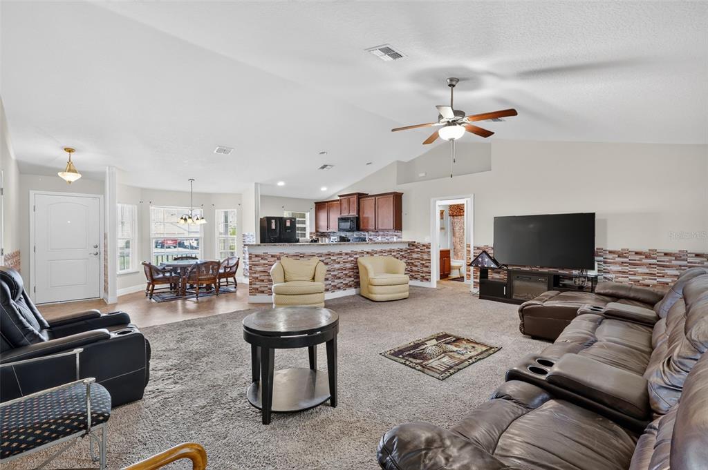 A living room with carpeted floors, a brown leather sectional, and an open kitchen area — 702 CHELSEA AVENUE, FRUITLAND PARK, FL