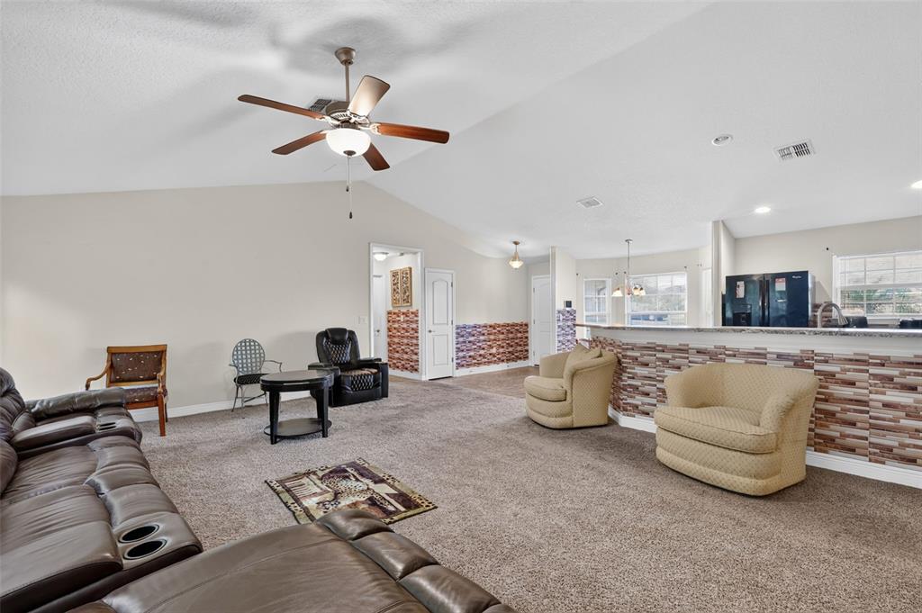 A living room features a vaulted ceiling, carpeted flooring, and a kitchen breakfast bar — 702 CHELSEA AVENUE, FRUITLAND PARK, FL