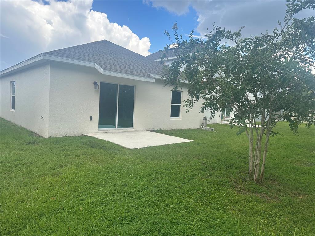 The exterior of a house features a concrete patio, sliding glass doors, and a small tree — 4439 TWISTED TWIG BEND, KISSIMMEE, FL