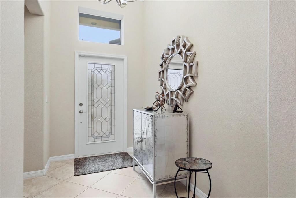 A bright entryway features a white front door, tiled floors, and a mirrored accent cabinet — 11702 ANHINGA AVENUE, VENICE, FL