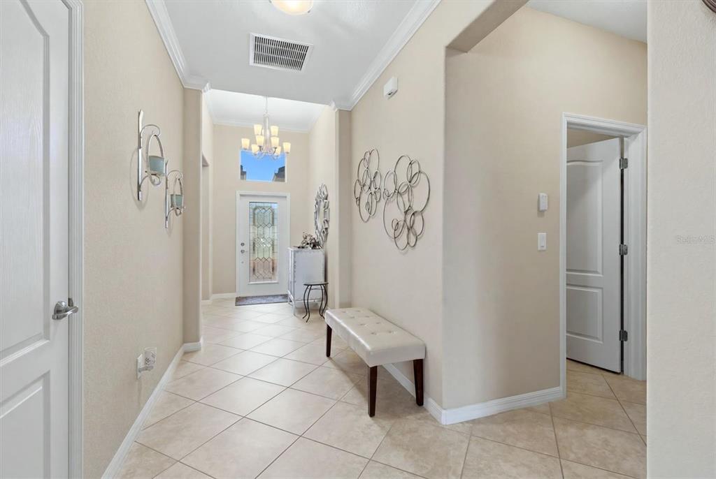 A bright entryway features tile flooring, a white bench, and a decorative chandelier — 11702 ANHINGA AVENUE, VENICE, FL