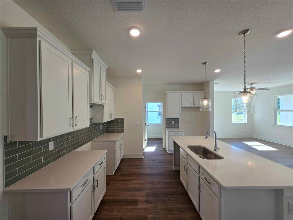 A modern kitchen features white cabinetry, a central island with a sink, and gray backsplash tile — 3352 DAYBREAK RUN LOOP, SPRING HILL, FL