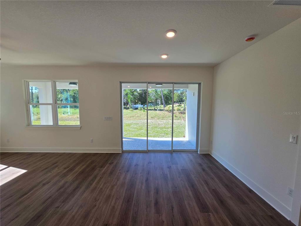 A living room with wood-look flooring, recessed lighting, and sliding glass doors to a backyard — 3352 DAYBREAK RUN LOOP, SPRING HILL, FL