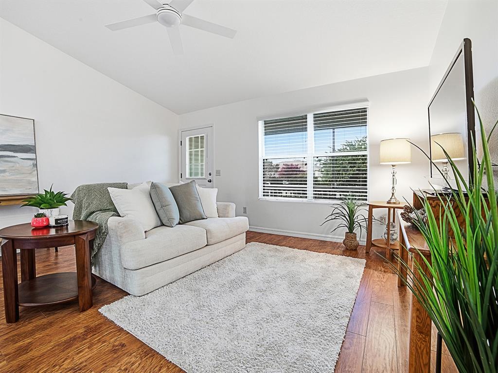 An open-concept living room features a white sofa, wood flooring, and a kitchen beyond — 1521 HOLLYBERRY PLACE, THE VILLAGES, FL