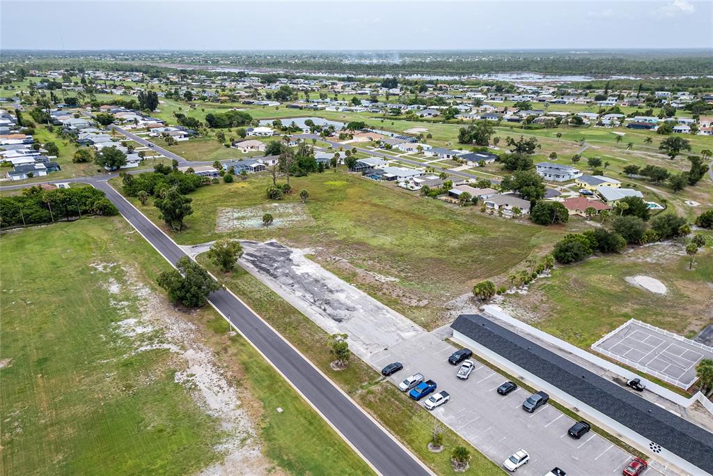 An aerial view shows a paved parking lot, a vacant grassy lot, and surrounding residential homes — 3 GOLFVIEW ROAD, ROTONDA WEST, FL