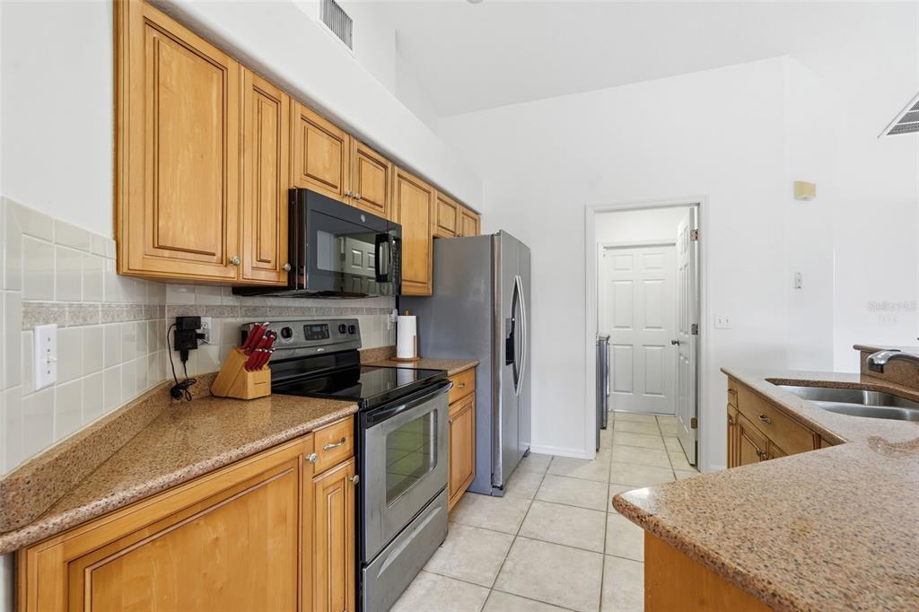 A kitchen features light wood cabinets, granite countertops, stainless steel appliances, and tile flooring — 2408 SW 53RD STREET, CAPE CORAL, FL