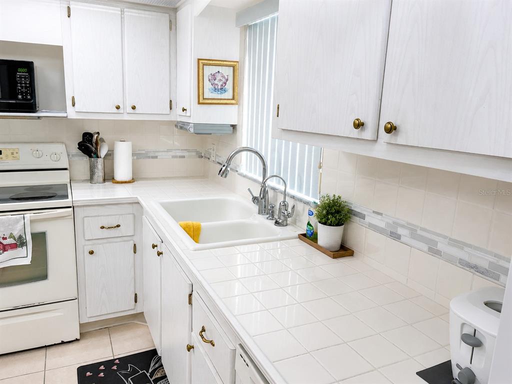A kitchen features white cabinets, tiled countertops, a double sink, and a white stove — 4575 COVE CIRCLE UNIT 506, ST PETERSBURG, FL