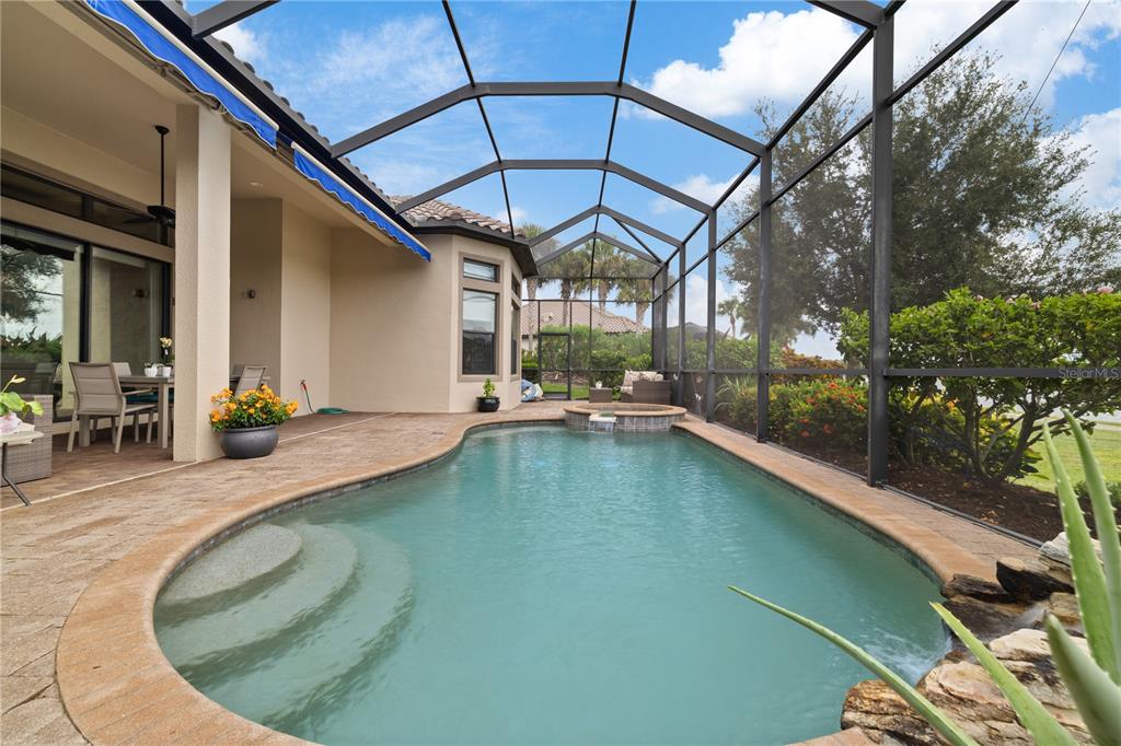A screened-in pool area with a spa, patio furniture, and a view of landscaping — 5311 BENITO COURT, BRADENTON, FL