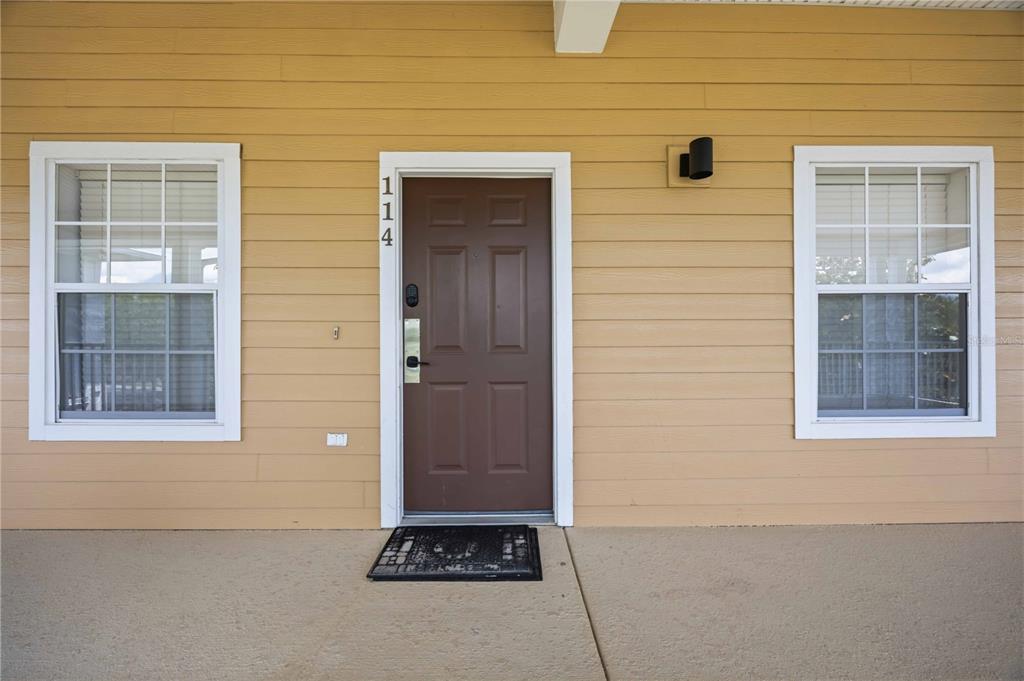 A brown front door with the number 114 is centered between two windows on a porch — 114 RUM RUN, DAVENPORT, FL