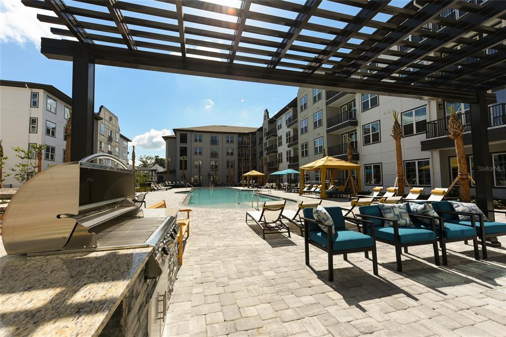 An outdoor pool area features a stainless steel grill, lounge chairs, and a wooden pergola — 6629 DAN DICIOLLA DRIVE UNIT A4, WILDWOOD, FL