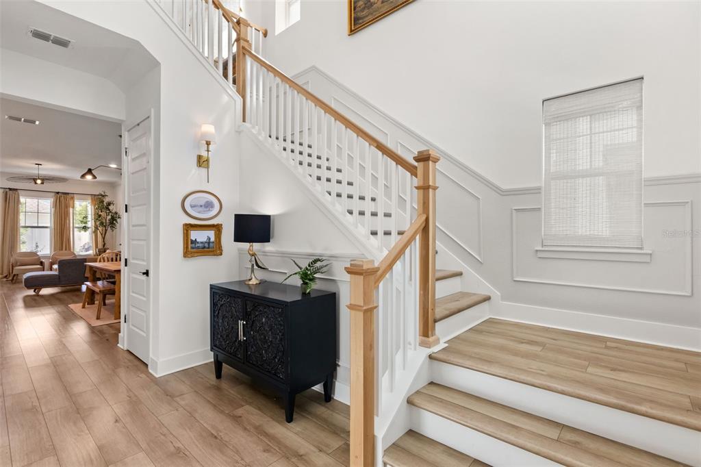 A bright entryway features a wooden staircase with white railings, light wood flooring, and wainscoting — 150 HAMMOCK PRESERVE LOOP, OAKLAND, FL