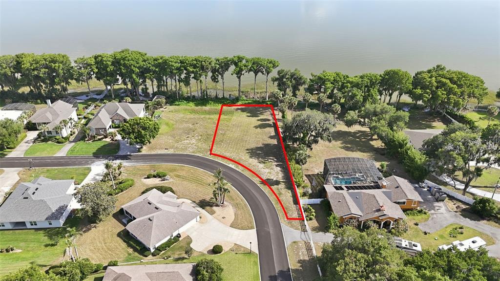 An aerial view shows a vacant waterfront lot outlined in red along a paved road — INDIAN TRAIL, EUSTIS, FL