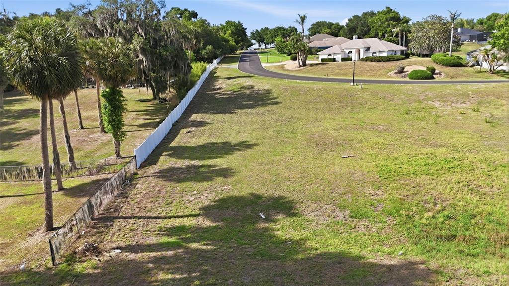 An aerial view shows a grassy residential lot bordered by a white fence and palm trees — INDIAN TRAIL, EUSTIS, FL