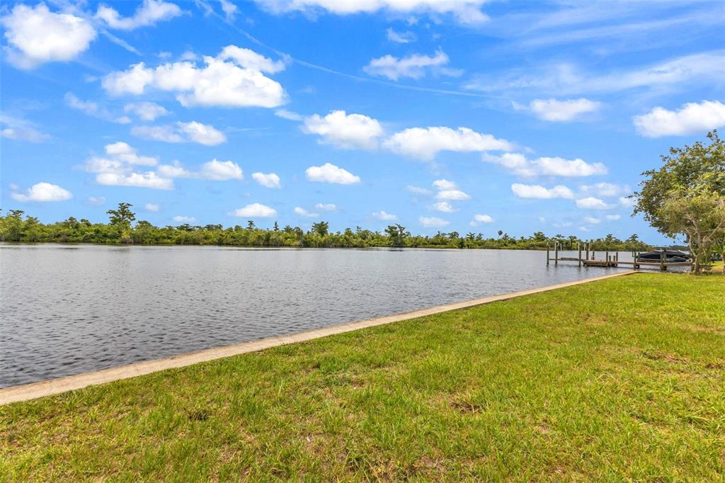 A grassy lawn slopes down to a calm lake with a small wooden boat dock — 10082 SW RIVERVIEW CIRCLE, ARCADIA, FL