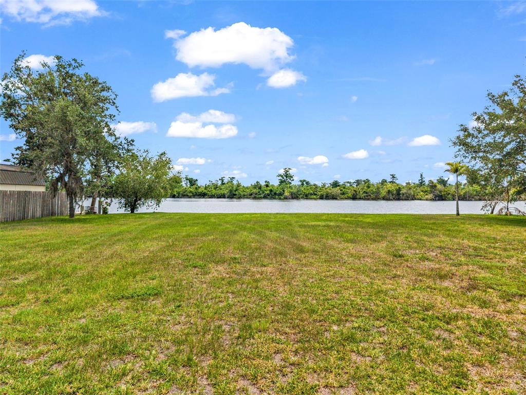A grassy backyard leads to a lake with a treeline in the background — 10082 SW RIVERVIEW CIRCLE, ARCADIA, FL