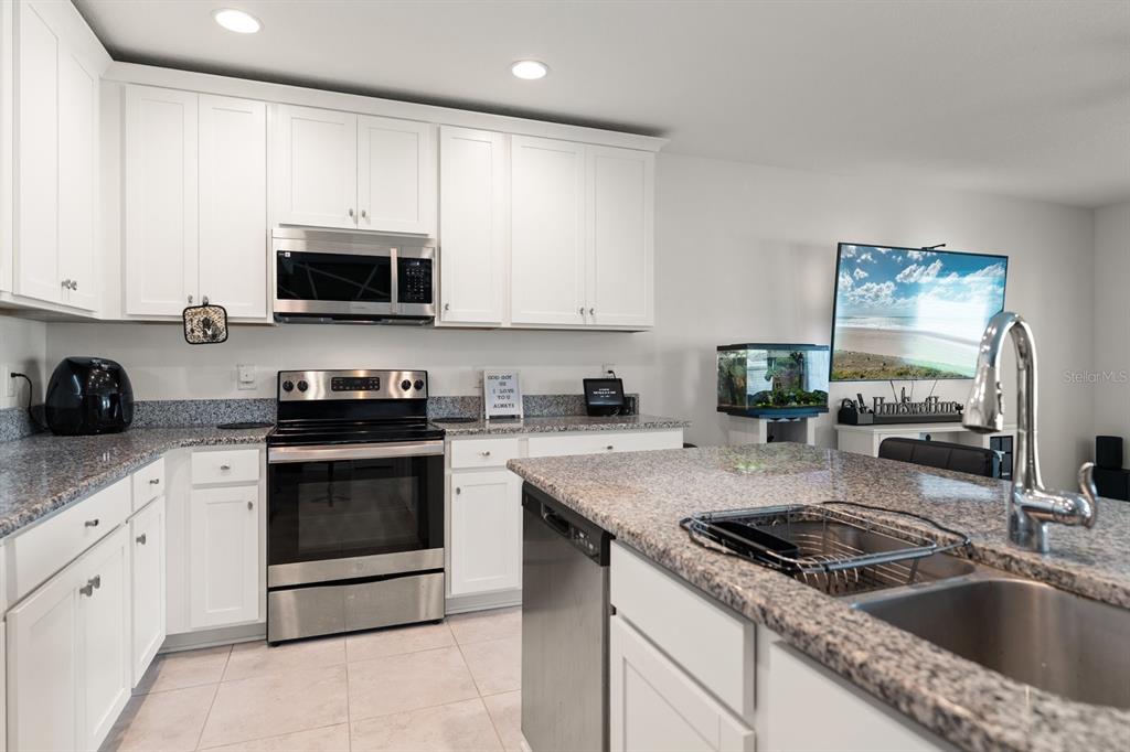 A modern kitchen features white cabinets, granite countertops, and walls with a geometric accent pattern — 13120 CONQUISTADOR LOOP, SPRING HILL, FL