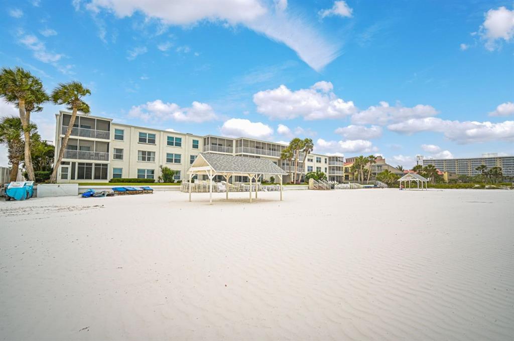 A multi-story apartment building sits behind a white sand beach with two wooden gazebos — 6154 MIDNIGHT PASS ROAD UNIT B04, SARASOTA, FL
