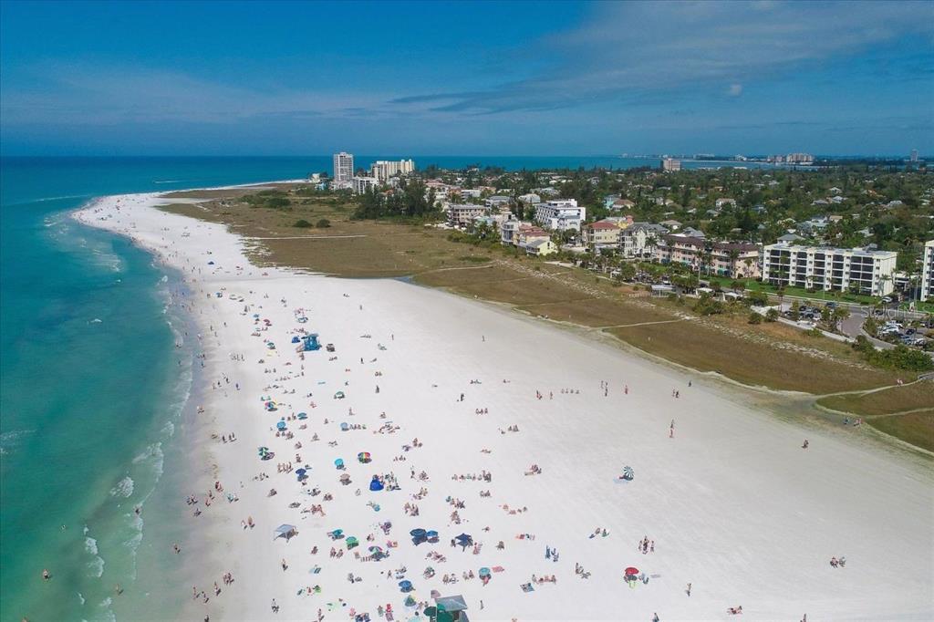 An aerial view shows a wide, sandy beach with people and buildings along the coast — 6154 MIDNIGHT PASS ROAD UNIT B04, SARASOTA, FL