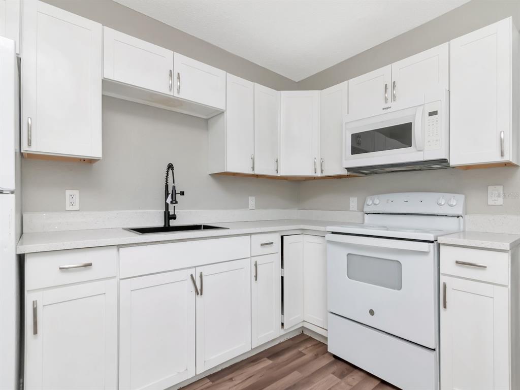 A kitchen features white cabinets, white countertops, a black faucet, and white appliances — 1209 62ND AVENUE E, BRADENTON, FL