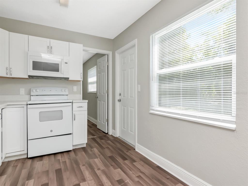 A kitchen features white cabinets, a white stove, a microwave, and wood-look flooring — 1209 62ND AVENUE E, BRADENTON, FL