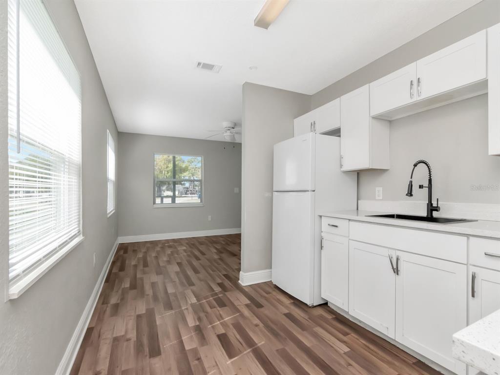 A kitchen with white cabinets and a white refrigerator opens into a dining area — 1209 62ND AVENUE E, BRADENTON, FL
