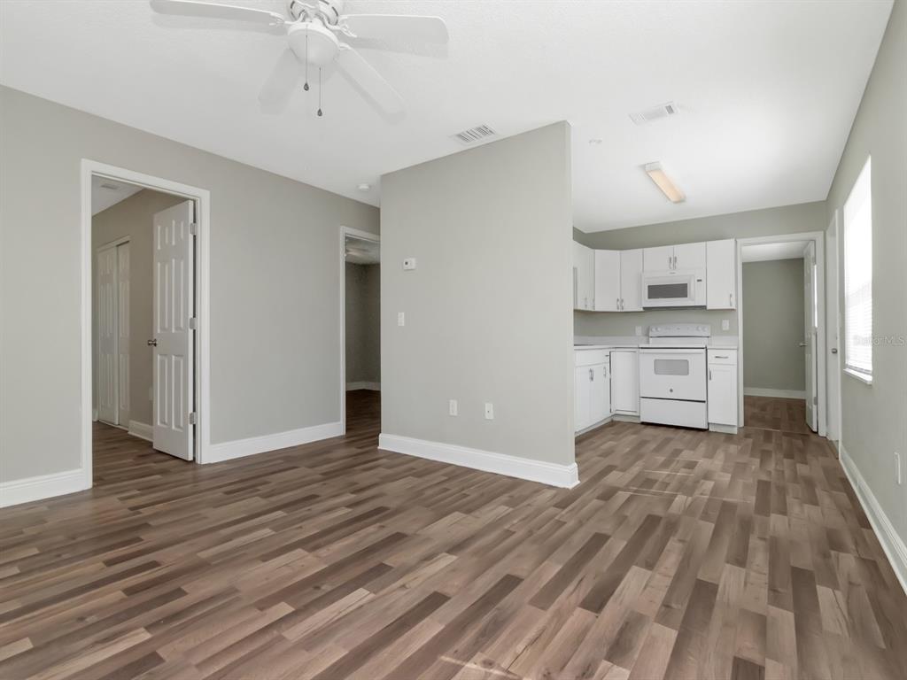 An open-concept living area with wood-look flooring leads into a kitchen with white appliances — 1209 62ND AVENUE E, BRADENTON, FL