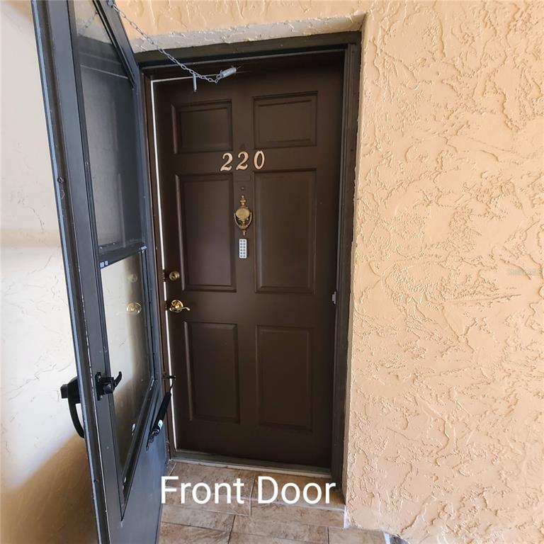 A brown front door with the number 220 is visible behind an open screen door — 220 BUTTONWOOD CIRCLE UNIT 220, SEMINOLE, FL