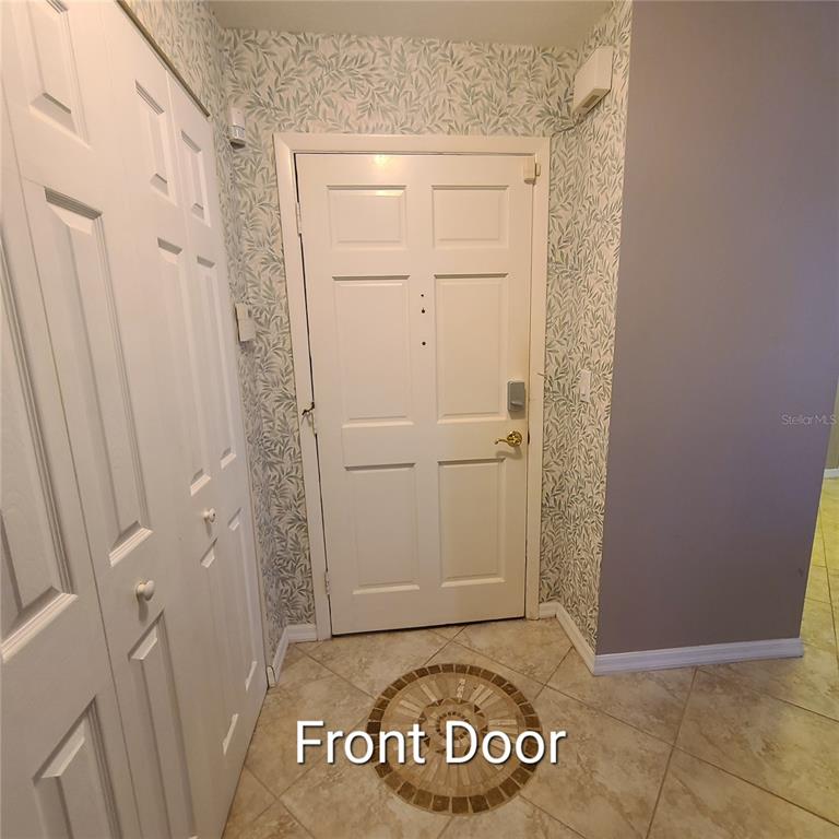 An entryway features a white front door, a closet with bifold doors, and patterned wallpaper — 220 BUTTONWOOD CIRCLE UNIT 220, SEMINOLE, FL