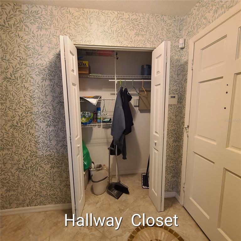 A hallway closet with bi-fold doors, wire shelving, and patterned wallpaper on the surrounding walls — 220 BUTTONWOOD CIRCLE UNIT 220, SEMINOLE, FL