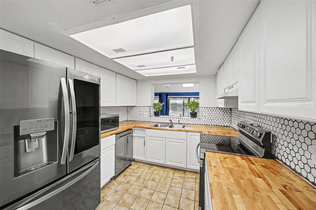 A kitchen with white cabinets, butcher block countertops, a hexagonal tile backsplash, and stainless appliances — 2008 HOUNDSLAKE DRIVE, WINTER PARK, FL