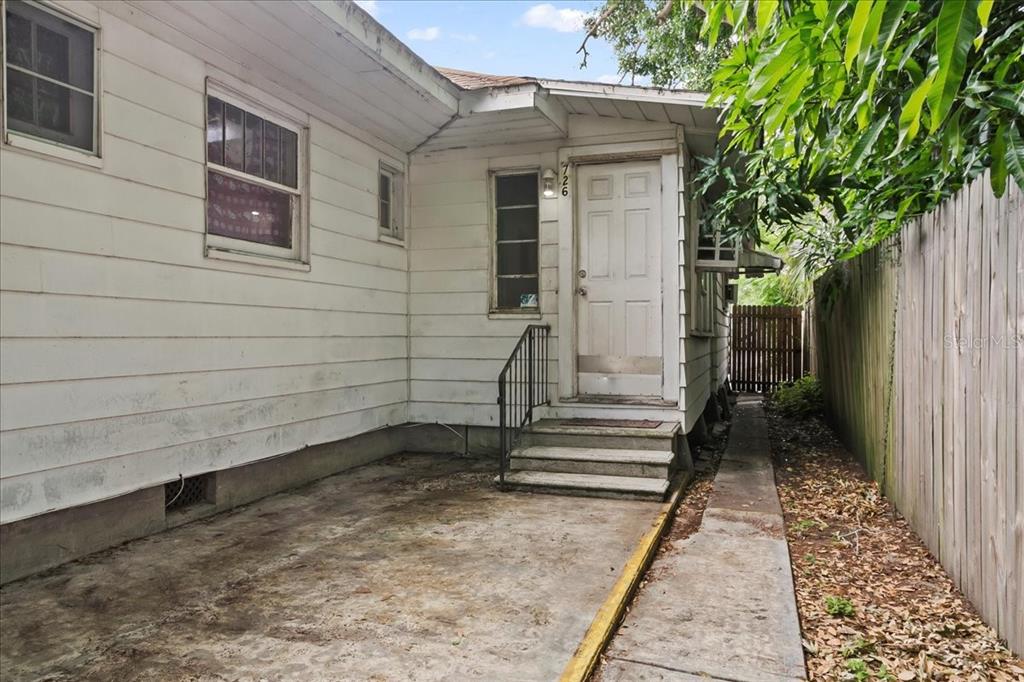 A white house exterior features a concrete patio, a small staircase, and a wooden fence — 724 W CENTRAL AVENUE, WINTER HAVEN, FL