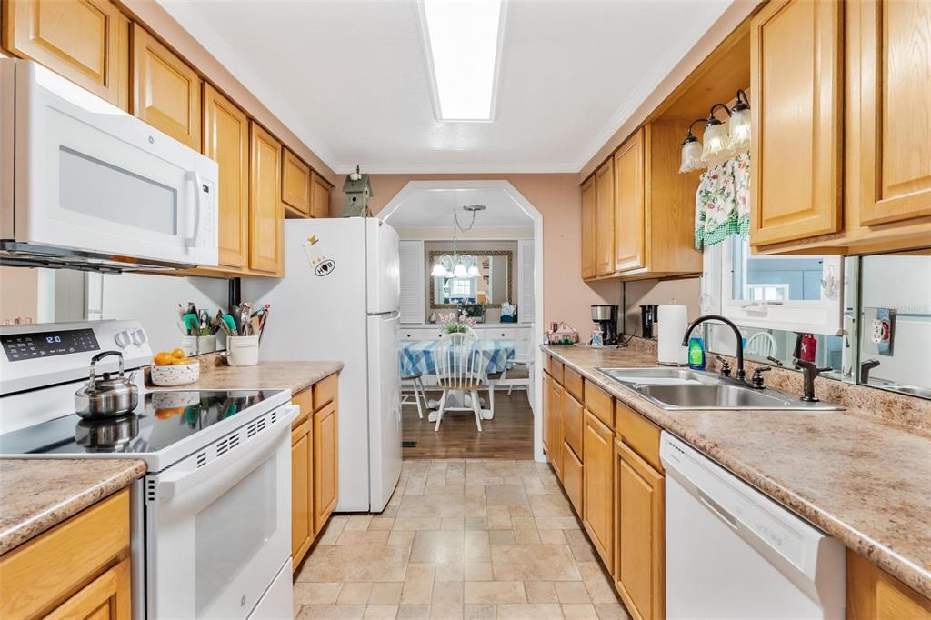 A kitchen with wood cabinets, laminate countertops, white appliances, and a view into the dining room — 2470 KAREN DRIVE, MOUNT DORA, FL