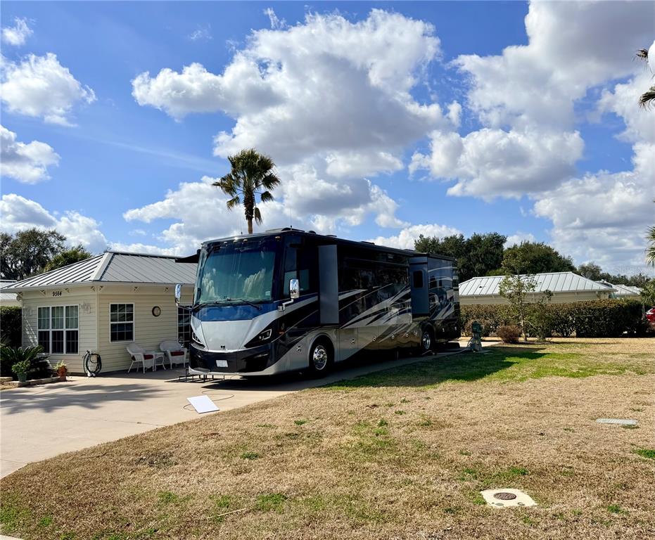 A large recreational vehicle is parked on a concrete driveway next to a small house — 9564 SE 47TH WAY, WEBSTER, FL