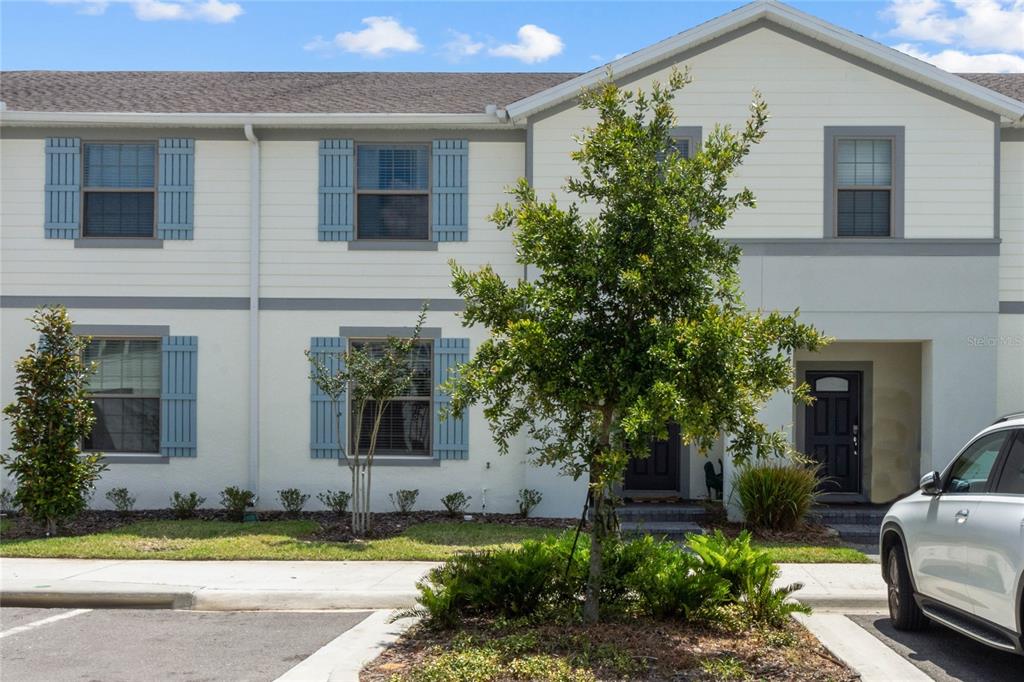 A two-story townhouse exterior with light siding, blue shutters, and a small front yard — 2431 DUBAI STREET, KISSIMMEE, FL