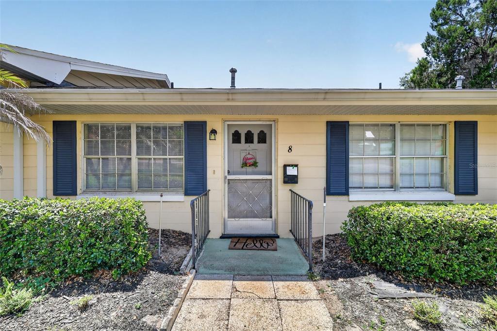 A single-story house exterior features yellow siding, blue shutters, and a central front entrance — 445 S GRANDVIEW STREET UNIT 8, MOUNT DORA, FL