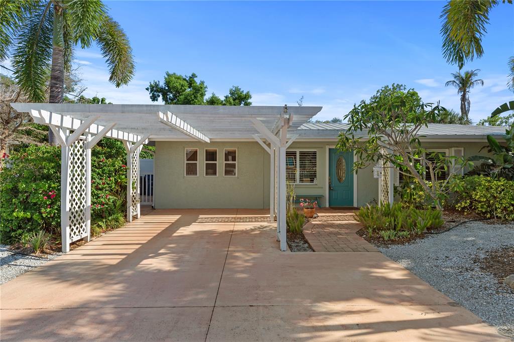 A single-story house with a white wooden pergola carport and a teal front door — 7860 HOLIDAY DRIVE, SARASOTA, FL