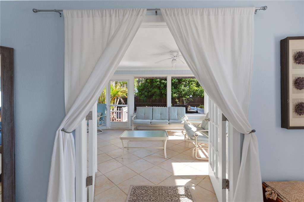 A sunroom with light blue walls and tile floors is viewed through white French doors — 7860 HOLIDAY DRIVE, SARASOTA, FL