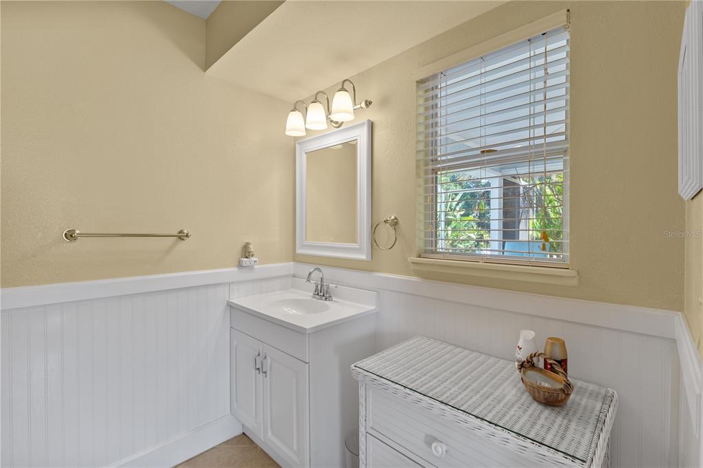 A bathroom features a white vanity, a mirror, a window with blinds, and beadboard wainscoting — 7860 HOLIDAY DRIVE, SARASOTA, FL