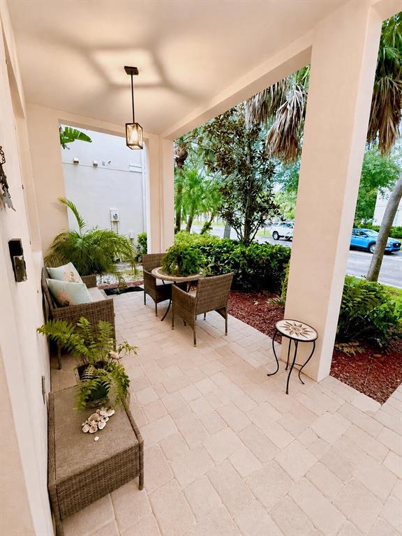 A covered patio features wicker furniture, a small round table, and light-colored stone pavers — 8074 MURANO CIRCLE, PALM BEACH GARDENS, FL