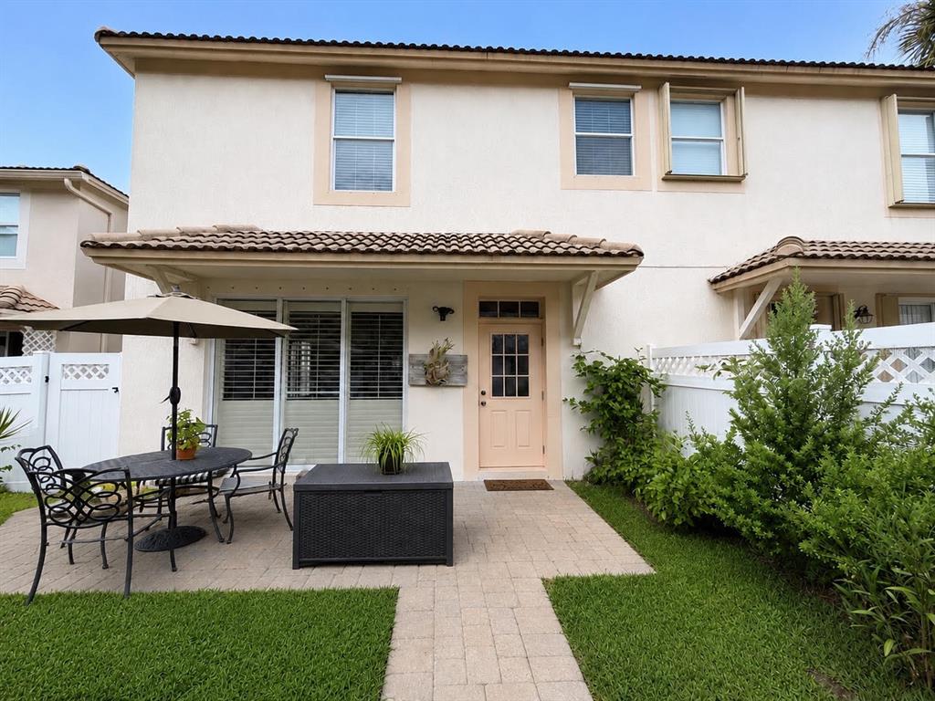 A patio with a dining set and storage box sits outside a two-story residential building — 8074 MURANO CIRCLE, PALM BEACH GARDENS, FL