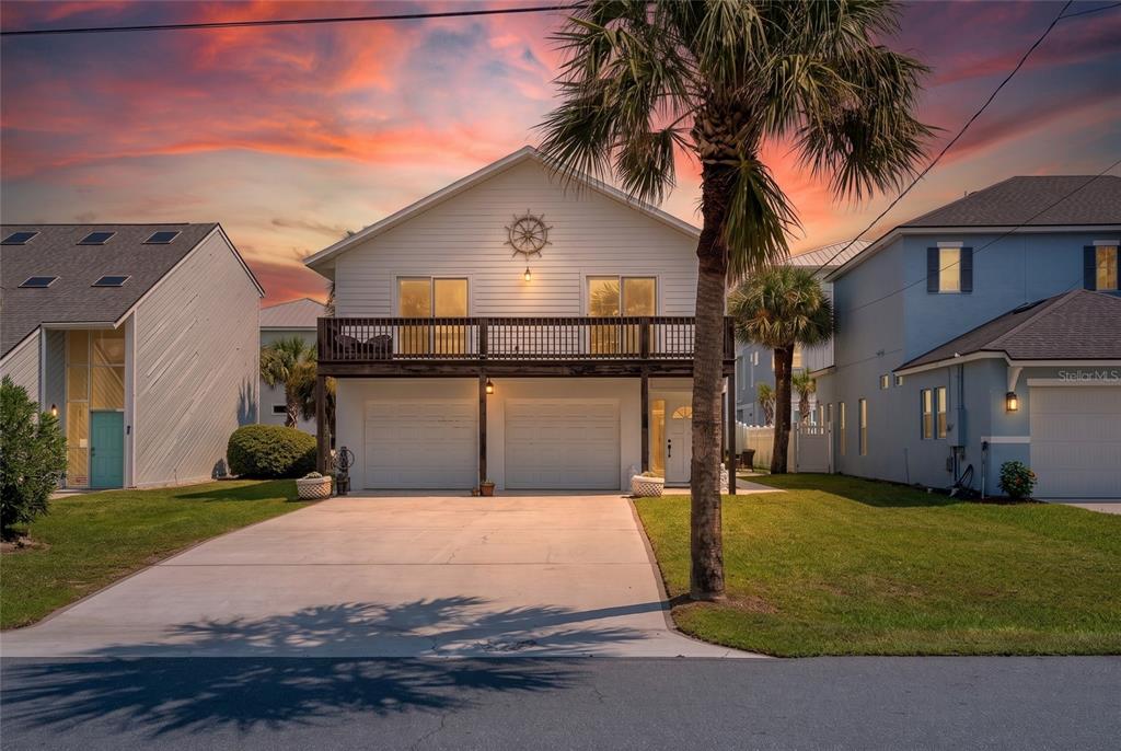 A two-story house with a balcony, two garage doors, and a palm tree in front — 712 CENTRAL AVE N, FLAGLER BEACH, FL